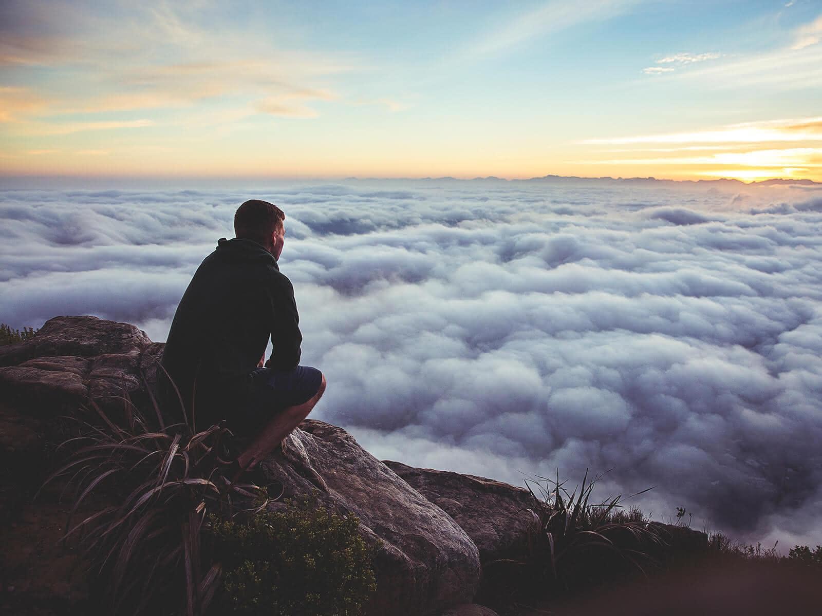Mann sitzt auf einem Felsen über den Wolken